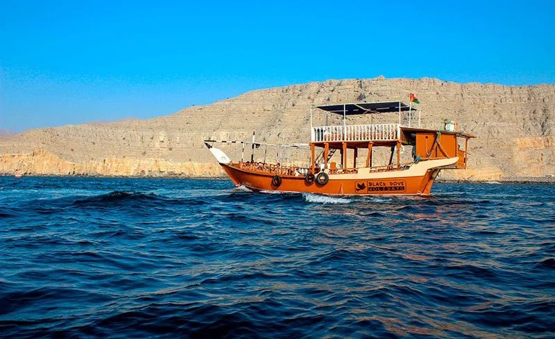 A dhow cruising between the cliffs of a Musandam fjord