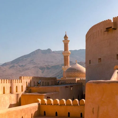 The walls and round tower of Nizwa Fort, with a mosque and mountains behind