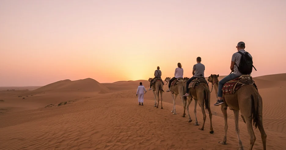 A camel caravan crossing the dunes at sunset
