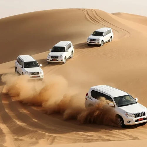 Four white 4x4s driving over dunes, throwing up sand