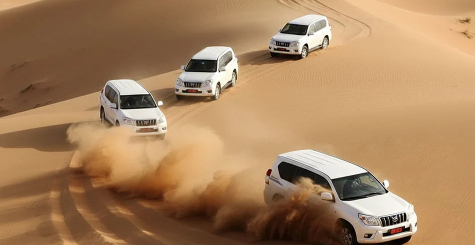 Four white 4x4s driving over dunes, throwing up sand