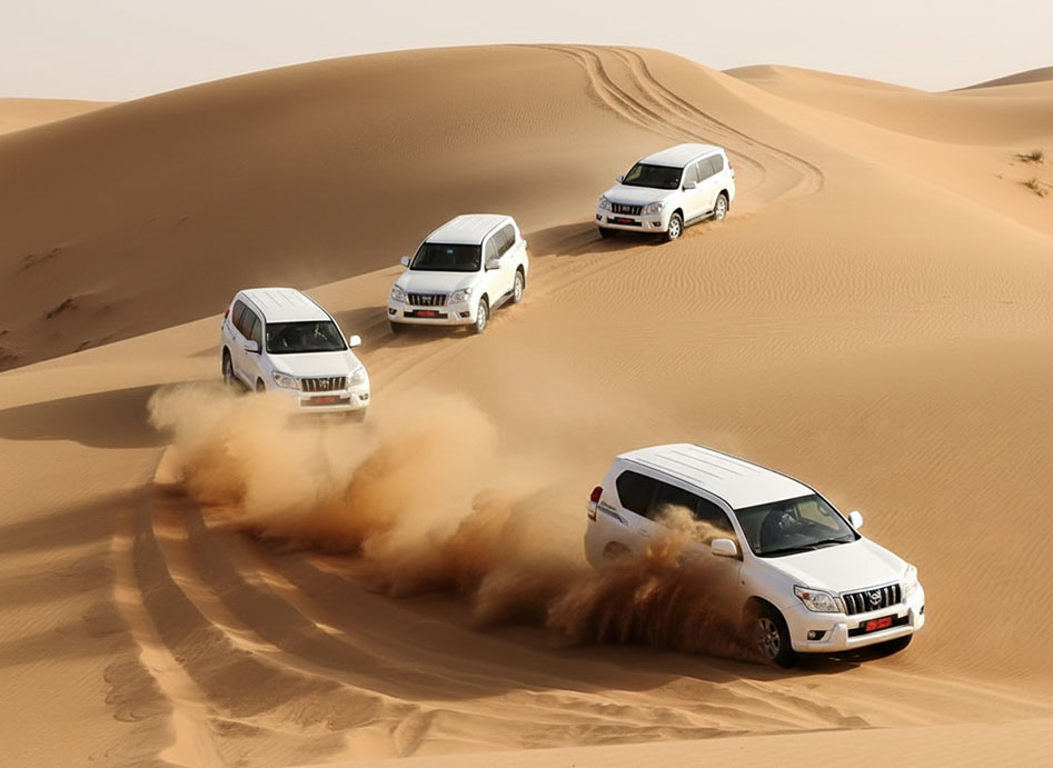 Four white 4x4s driving over dunes, throwing up sand