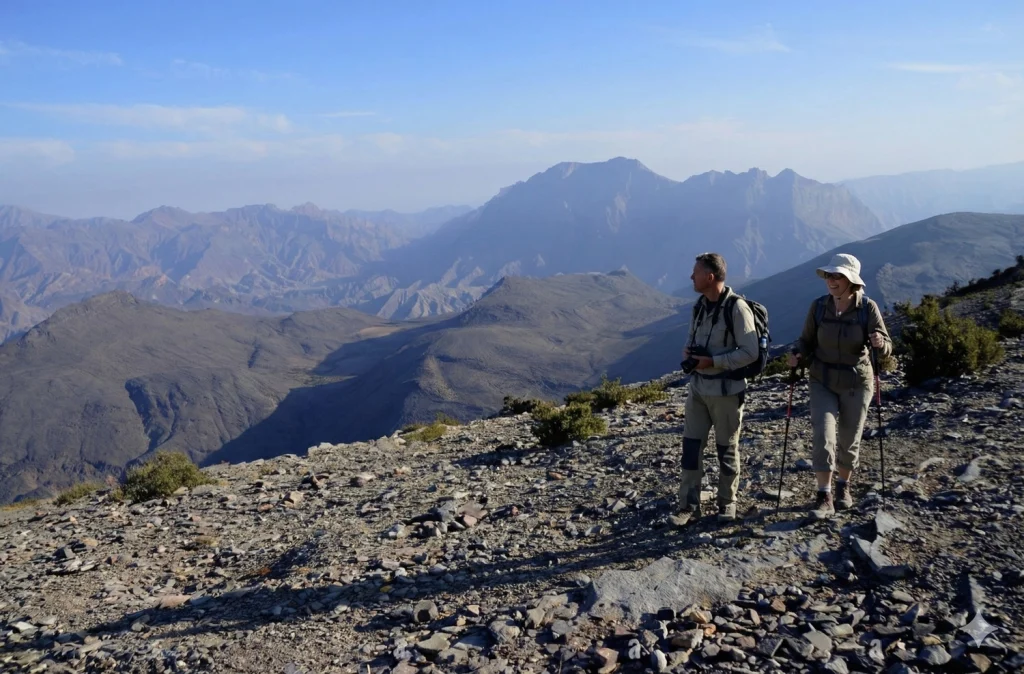 Two hikers on a rocky ridge with mountains behind