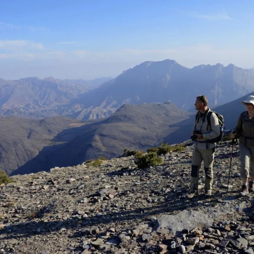 Two hikers on a rocky ridge with mountains behind