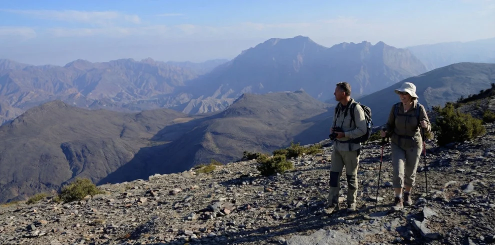 Two hikers on a rocky ridge with mountains behind