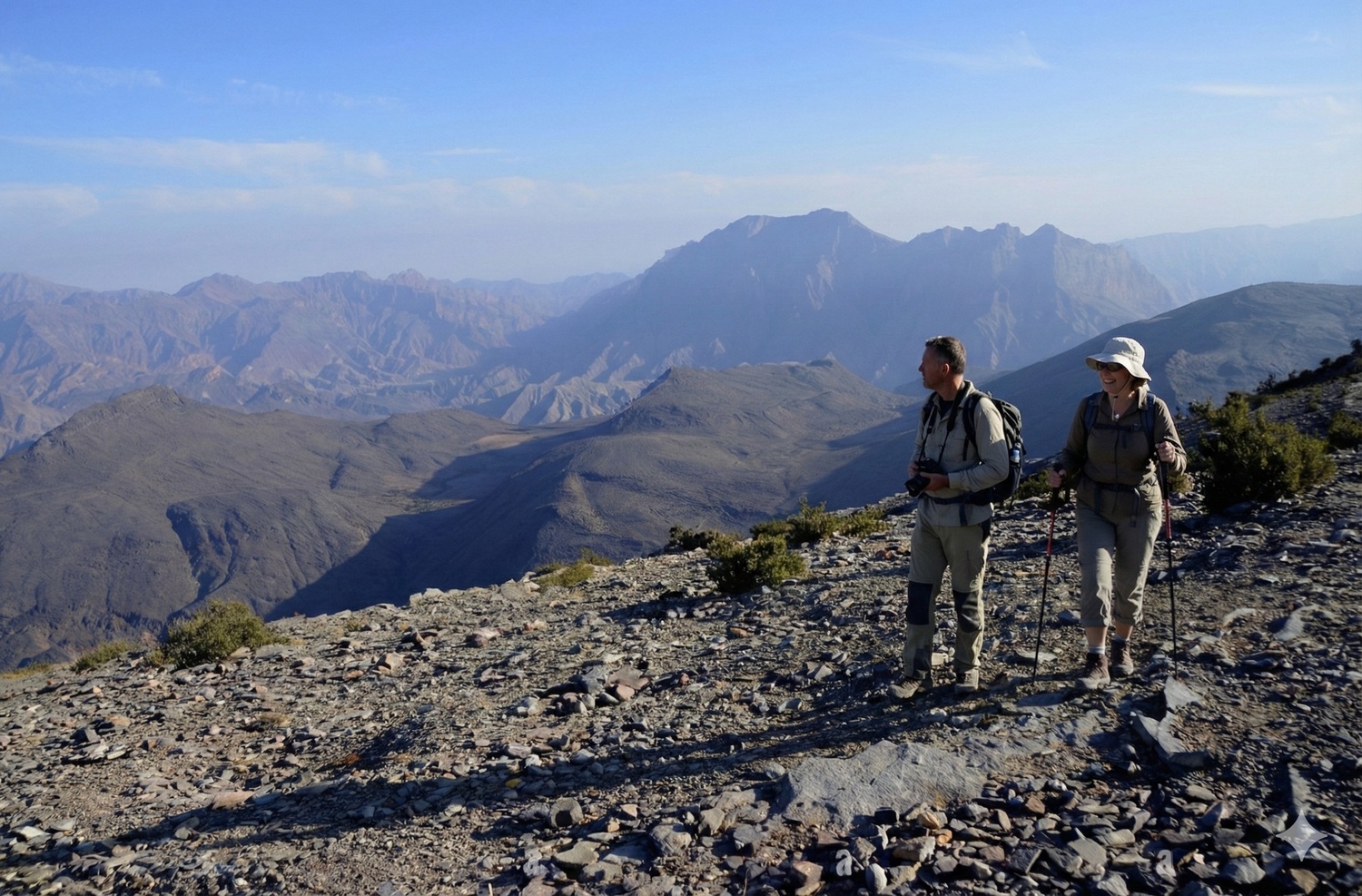 Two hikers on a rocky ridge with mountains behind