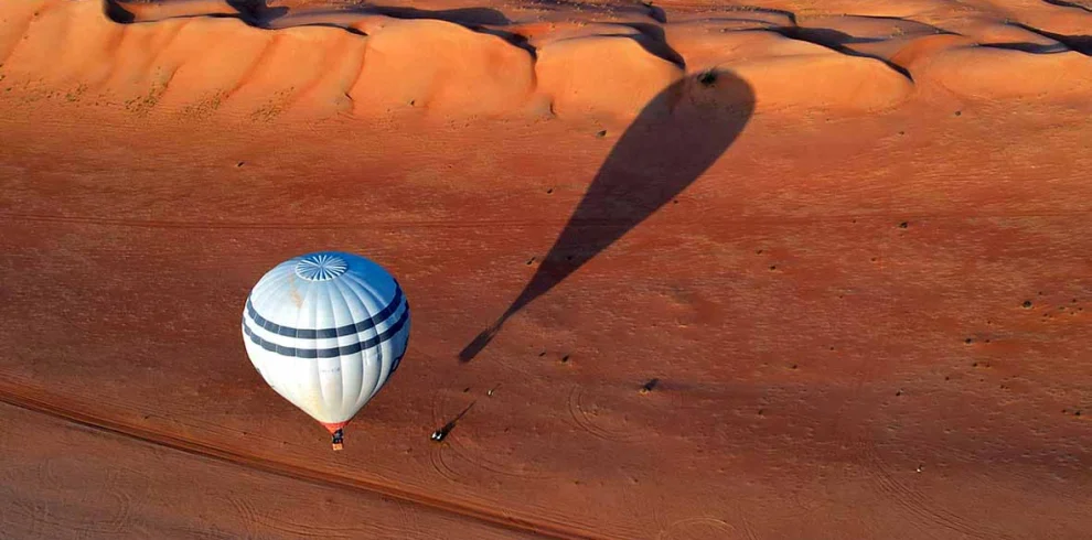 A hot-air balloon and its shadow over orange dunes