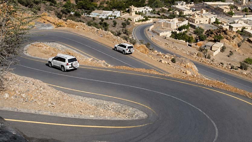 Two 4x4 vehicles on a winding mountain road above a village