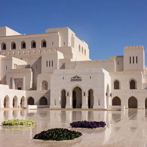 The white facade of the Royal Opera House Muscat with flower beds in front