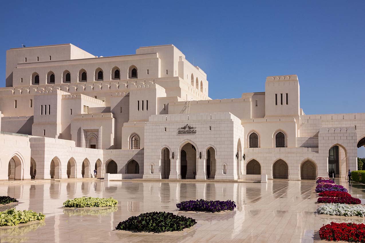 The white facade of the Royal Opera House Muscat with flower beds in front