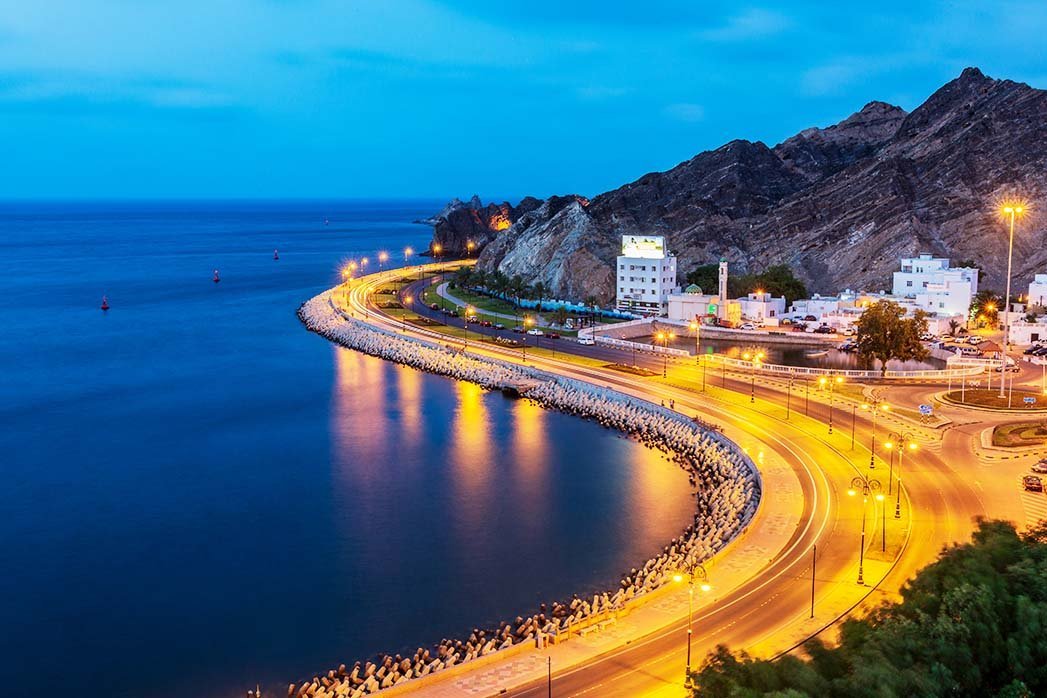 Mutrah Corniche lit up at dusk, with the sea and mountains behind