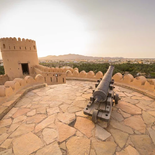 A cannon on the stone terrace of Nakhal Fort, with a watchtower