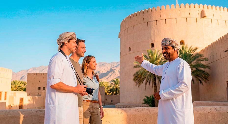 A guide in traditional dress talking with three visitors outside a fort
