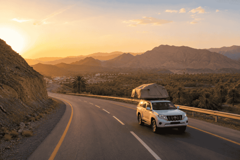 White 4x4 with a rooftop tent driving along a mountain road at sunset