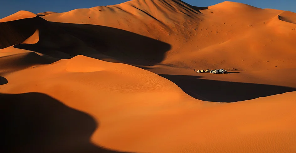 Tall orange dunes in the Empty Quarter, with a camp far below