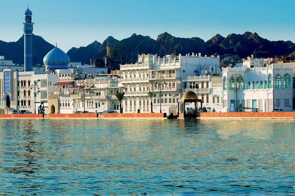 Houses and a mosque along the Mutrah Corniche, with mountains behind