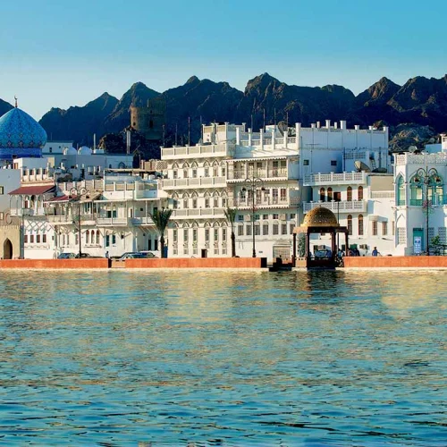 Houses and a mosque along the Mutrah Corniche, with mountains behind