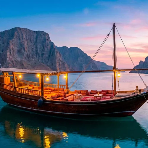 A dhow lit up at dusk in a fjord between steep cliffs