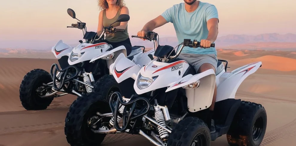 Two riders on quad bikes in the dunes