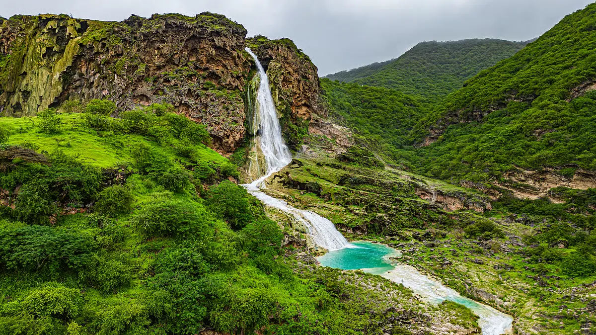 A waterfall and turquoise pool among green hills near Salalah in the khareef