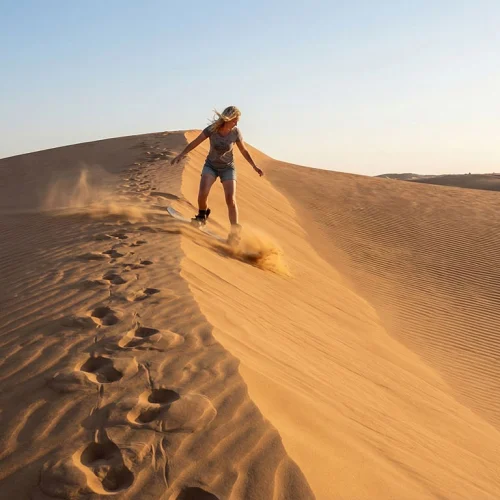 A sandboarder riding down a dune