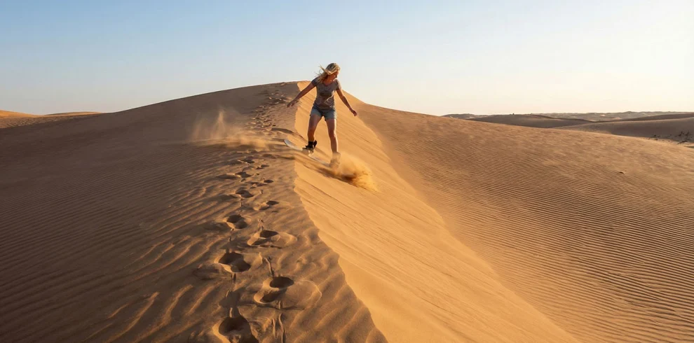 A sandboarder riding down a dune