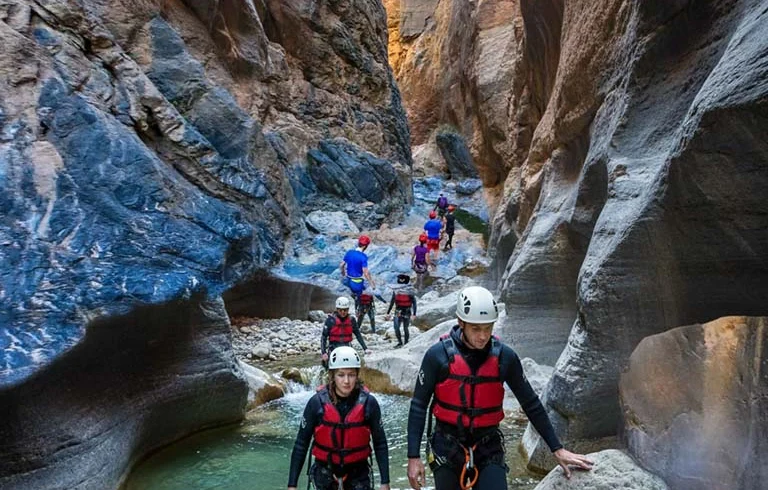 People in helmets and life jackets wading through a narrow canyon