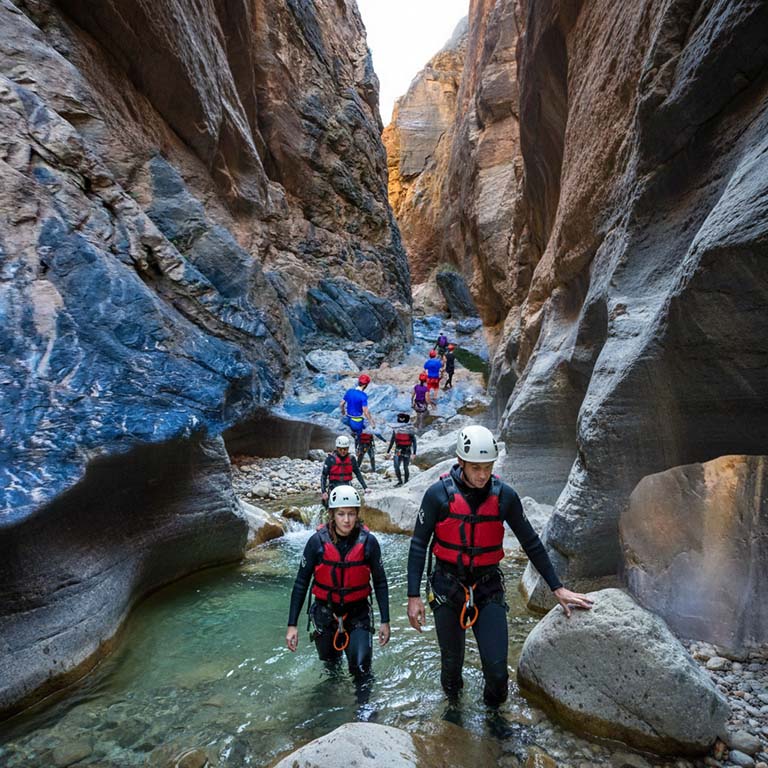 People in helmets and life jackets wading through a narrow canyon