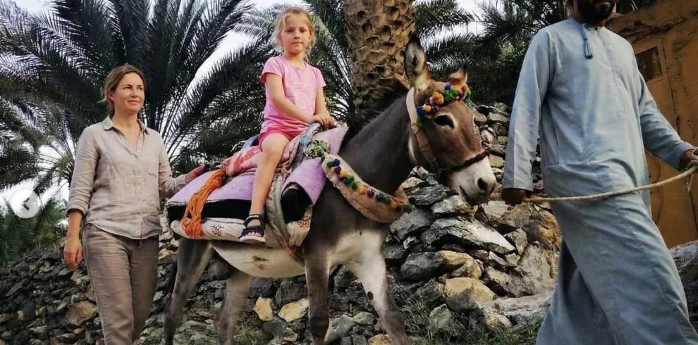 A child riding a donkey, led by a guide among palms