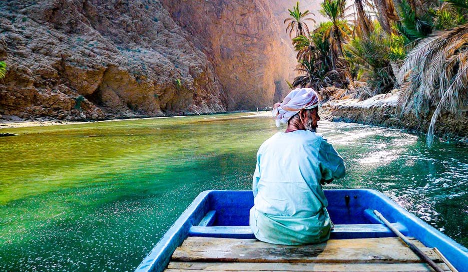 A guide in a small boat on the green pools of Wadi Shab