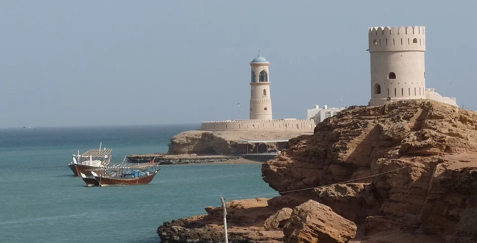 Watchtowers and a lighthouse on a rocky shore, with dhows at anchor